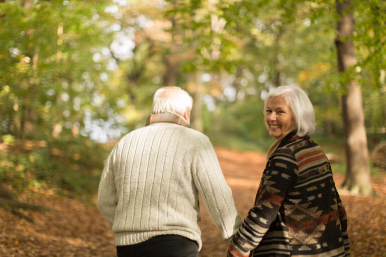 Portrait smiling senior couple holding hands and walking in autumn park